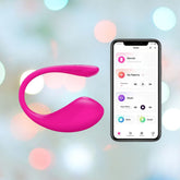 A pink wearable device, the Lovense Lush 3 Egg Vibrator by Lovense, is shown next to a smartphone displaying its control interface. The smartphone screen shows options for remote control, custom patterns, music sync, alarm, and sound effects. The background features a soft setting with colorful bokeh lights.